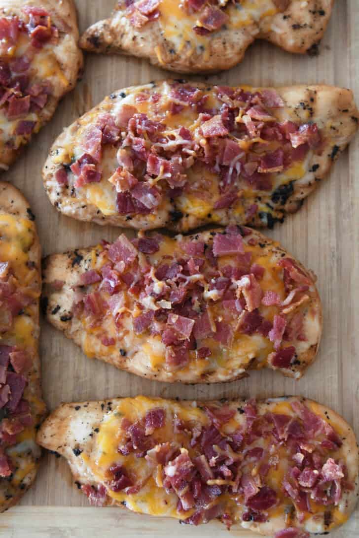 Cooked chicken breasts on cutting board with melted cheese and cooked bacon.