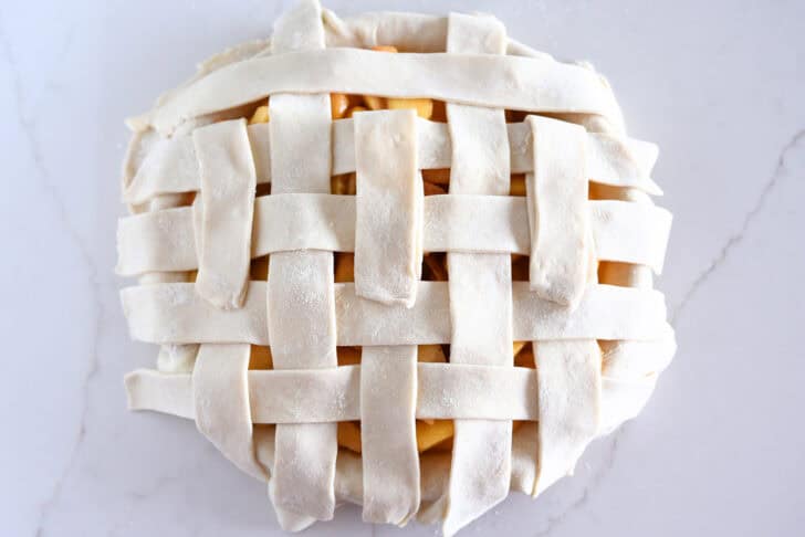Assembling lattice pie crust on fresh peach pie.