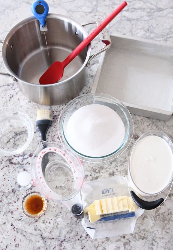 Caramel making supplies all laid out: pot, spatula, sugar, cream, butter, vanilla, thermometer.