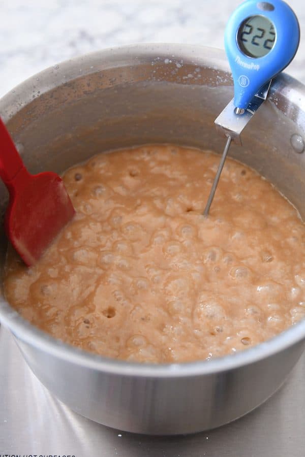 Cooking caramels to 245 degrees in a metal pot with a red spatula stirring it.