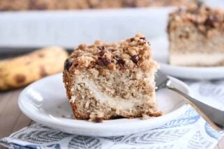Piece of banana cream cheese coffee cake with chocolate chip streusel on white plate.