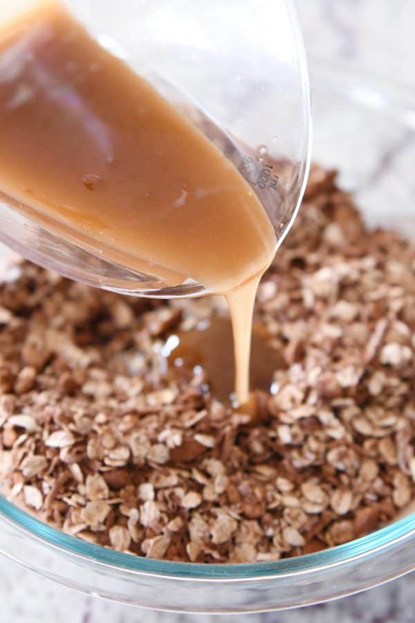 Pouring syrup onto dark chocolate brownie granola bar ingredients.