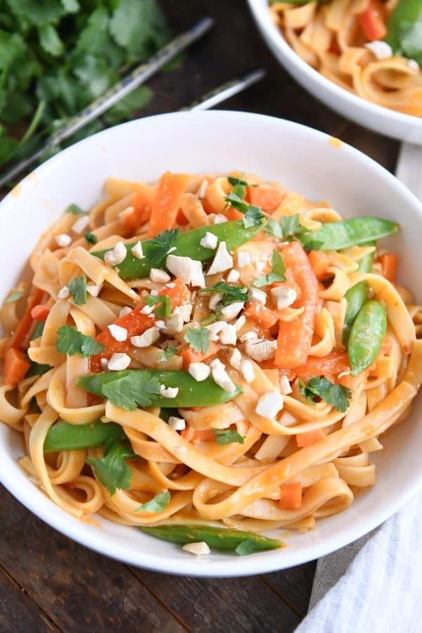 Instant Pot red coconut curry noodles in white bowl with chopped peanuts.