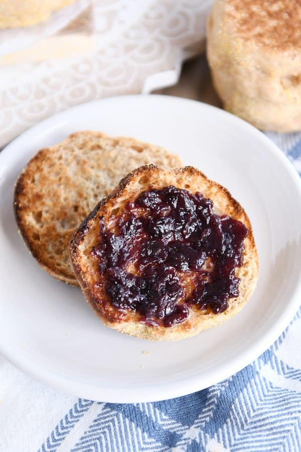 Split open easy homemade english muffin with butter and jam on white plate.