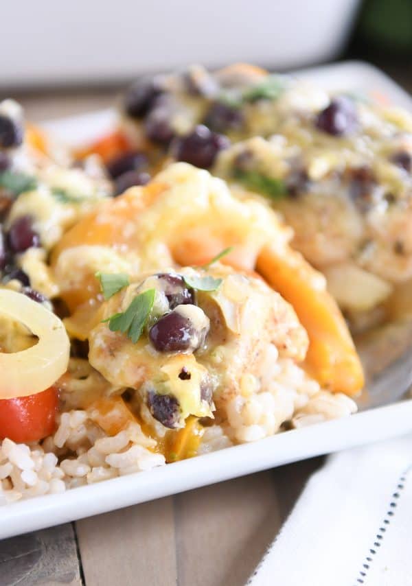 Cheesy chicken enchilada bake over brown rice on white platter.