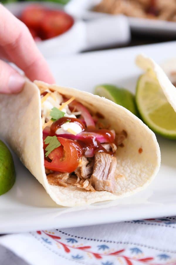 Holding taco made from instant pot bbq pork taco meat and pickled onions and drizzled with bbq sauce.