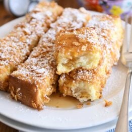 crunchy baked french toast sticks on white plate with powdered sugar and syrup