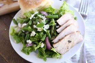 grilled pork salad with pork, red onions, green beans and roll on white plate