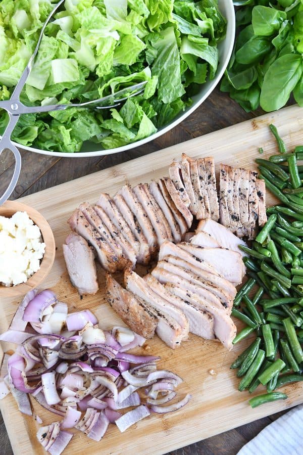 Top down view of grilled pork, grilled onions, grilled green beans, and feta cheese.