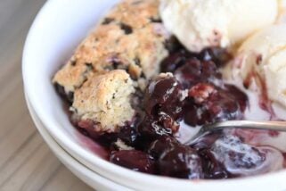 serving of cherry chocolate cobbler with chocolate chunk biscuit and vanilla ice cream in white bowl