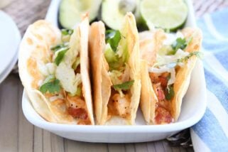 three crispy shrimp tacos in flour tortillas with lettuce on white tray