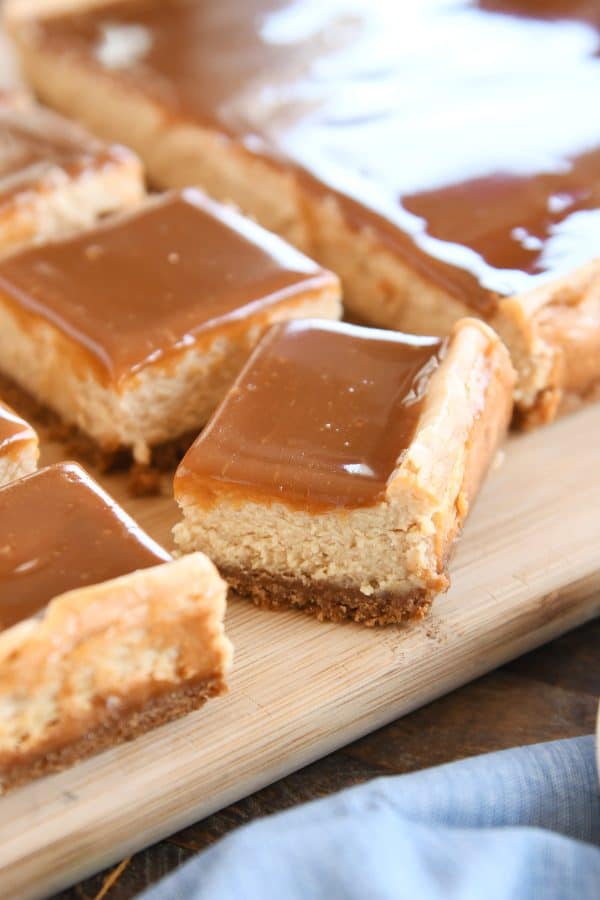 Squares of dulce de leche cheesecake bars cut on wood cutting board.