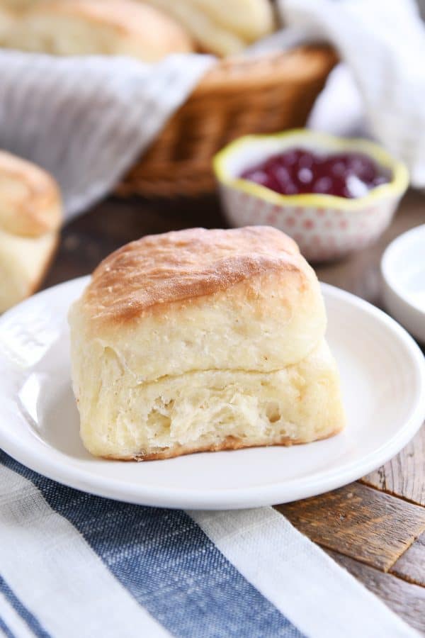 Super fluffy dinner roll on white plate on white and blue napkin.