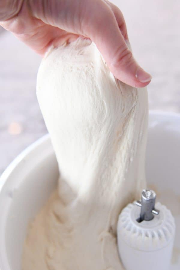 Pulling up bread dough out of mixer with hand.