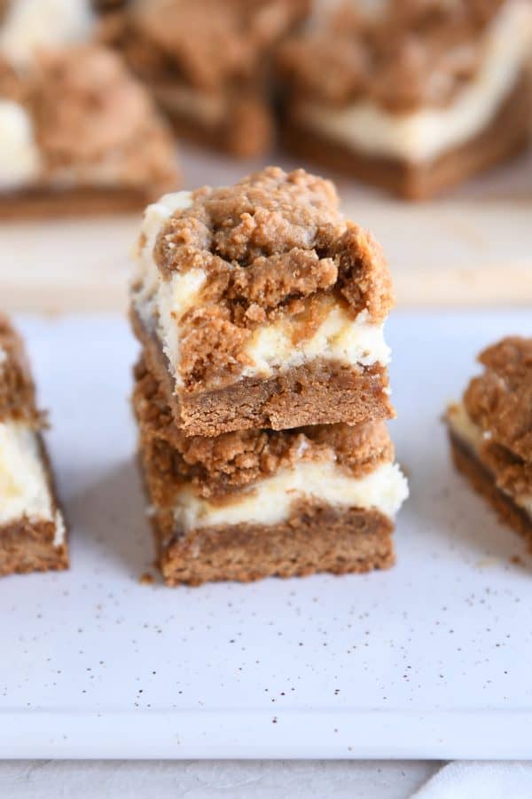 Two gingerbread cookie cheesecake bars stacked on top of each other on white tray.