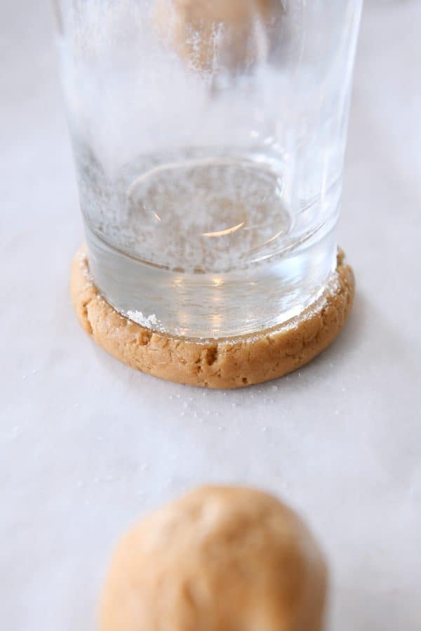 Pressing ball of gingerbread sugar cookie dough with glass coated in sugar.