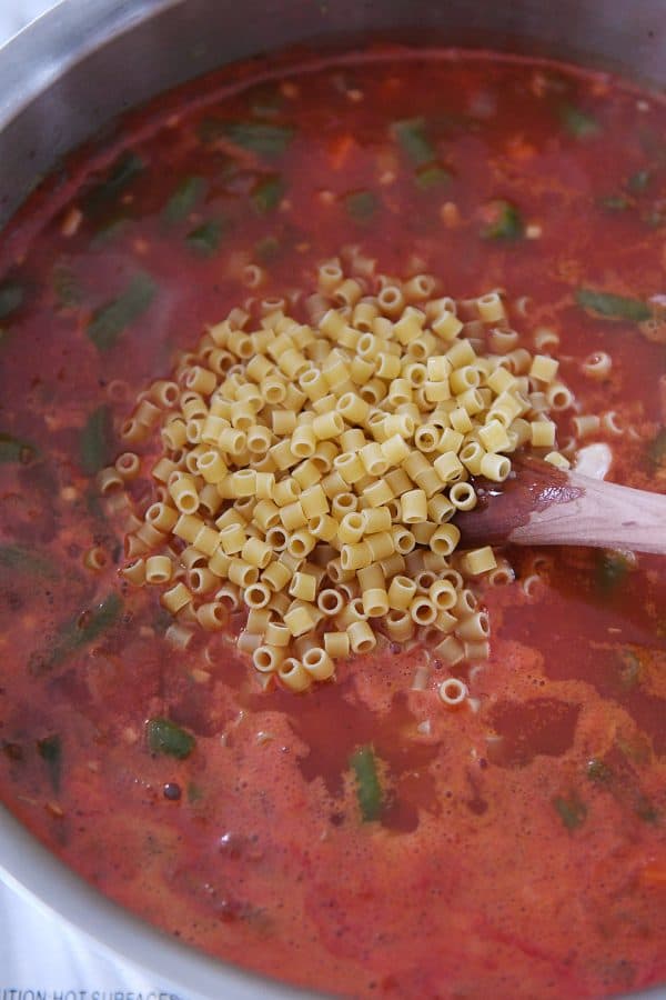 Ditalini pasta in pan of broth, tomatoes and vegetables.