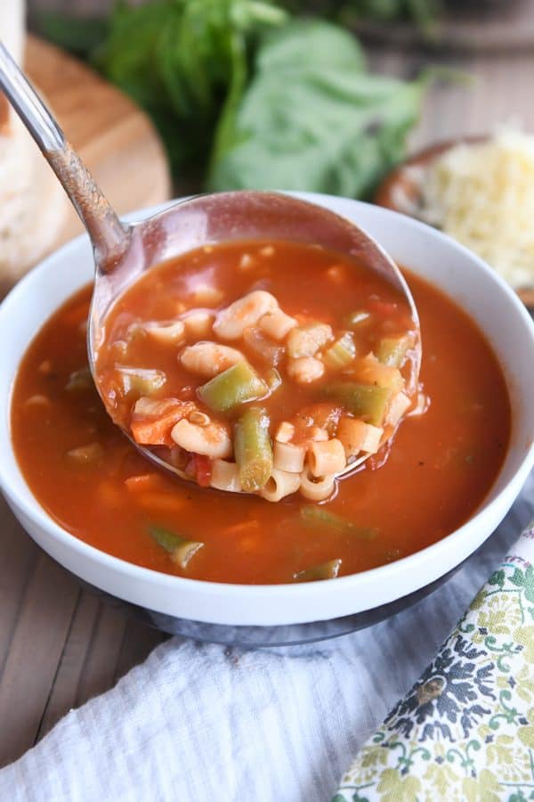 Ladle of minestrone soup being poured into ceramic bowl.