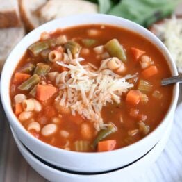 minestrone soup in two stacked white bowls with parmesan cheese
