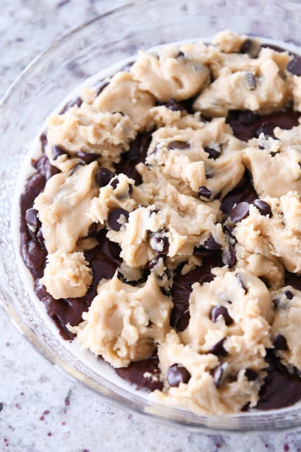 Clumps of cookie dough on top of brownie batter in pie plate.