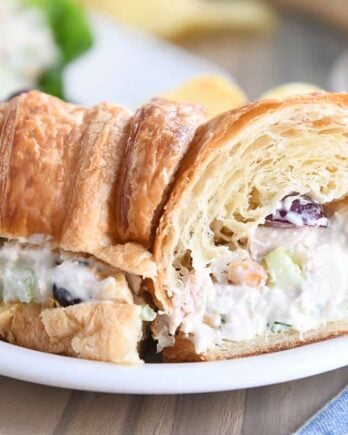 chicken salad sandwich on croissant cut in half on white plate with other half sandwich