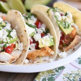 three fish tacos in corn tortillas on white platter