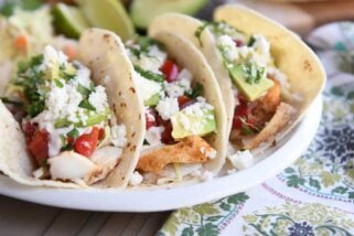 three fish tacos in corn tortillas on white platter