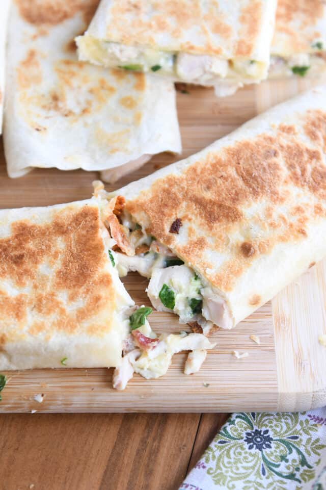 Two halves pulling apart of crispy chicken bacon ranch wrap on wood cutting board.