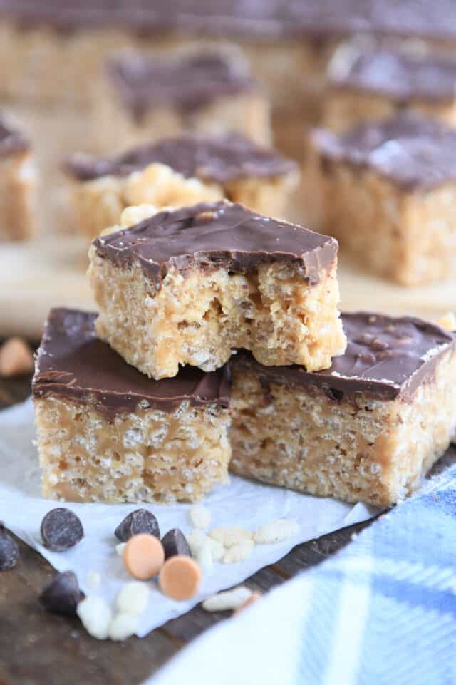 One scotcheroo with bite taken out stacked on top of two other scotcheroo bars on white parchment paper.