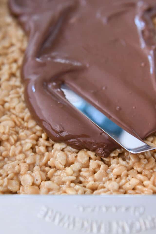 Spreading melted chocolate on scotcheroos in 9X13-inch pan.