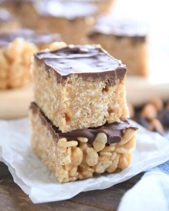 two scotcheroos stacked on white parchment with butterscotch and chocolate chips sprinkled around