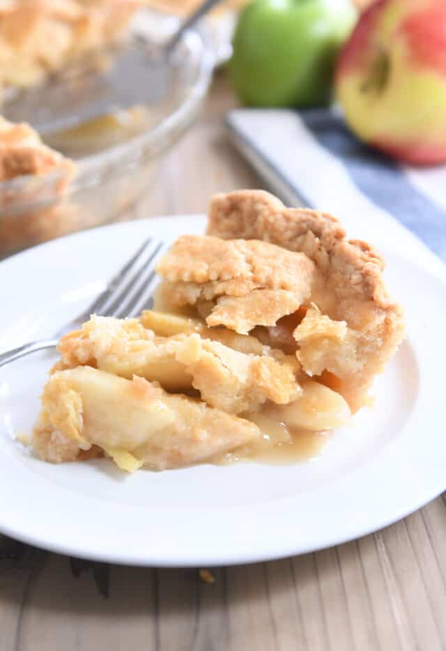Slice of apple pie with lattice crust on white plate.