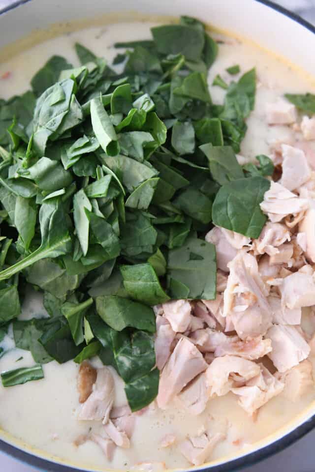 Spinach and cooked chicken in blue pot with chicken gnocchi soup ingredients.