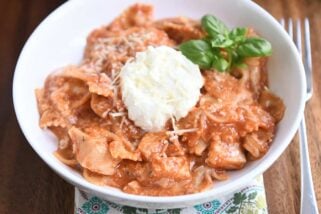 serving of chicken lasagna in white bowl with spoonful of ricotta and fresh basil leaves