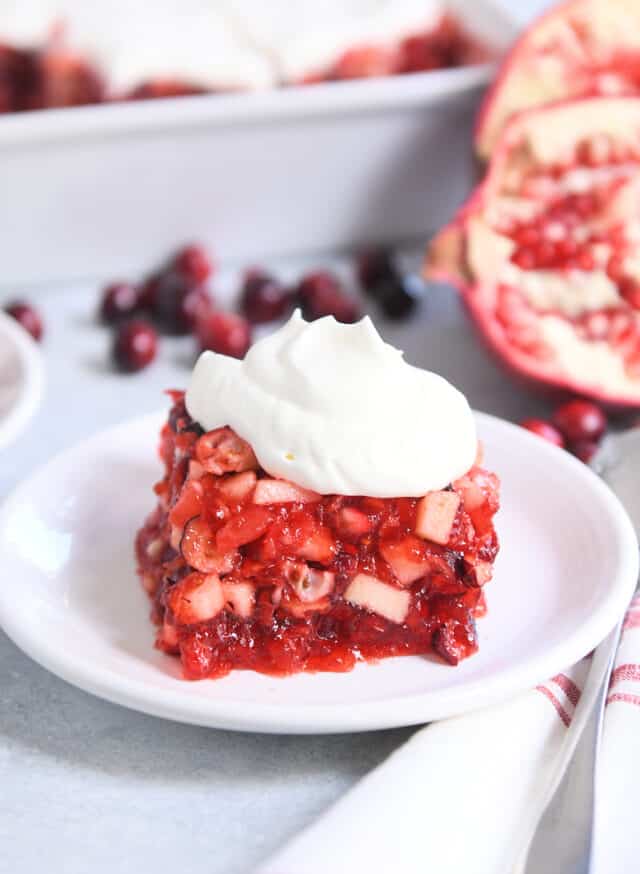 Square of cranberry pomegranate salad on white plate with dollop of sweet whipped topping.