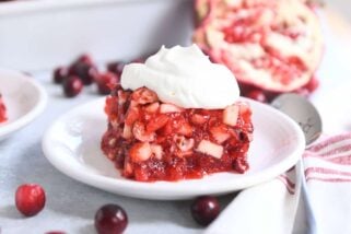 square of cranberry pomegranate jello salad on white plate with whipped topping