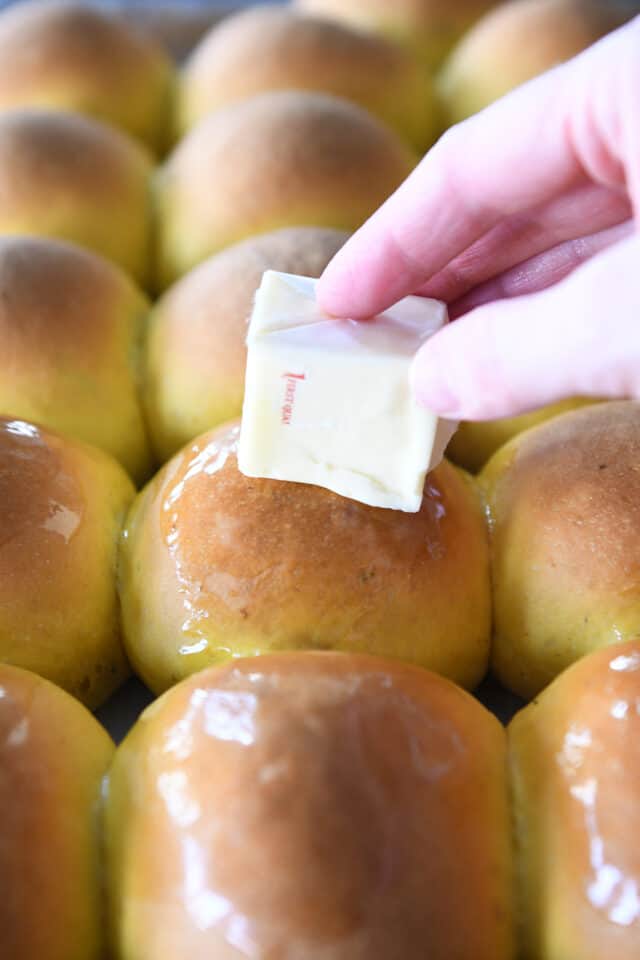 Rubbing cube of butter on warm fluffy pumpkin dinner rolls.