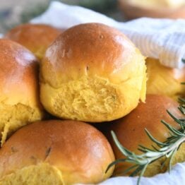 basket of several pumpkin dinner rolls with spring of fresh rosemary