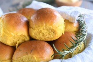 basket of several pumpkin dinner rolls with spring of fresh rosemary