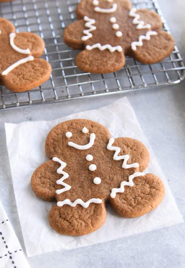 Soft gingerbread person cookie on piece of white parchment paper decorated with icing.