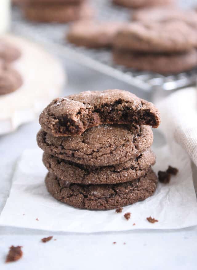 Bite taken out of chocolate ginger molasses cookie on stack of three whole cookies.
