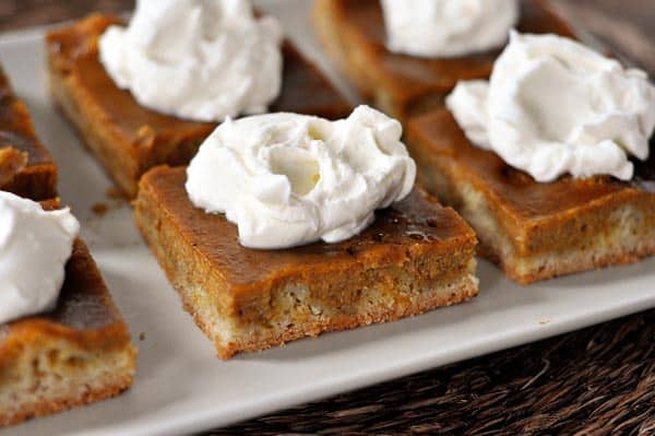 Pieces of pumpkin pie sheet cake with whipped topping on top on a white platter.
