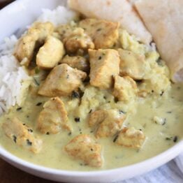 basil chicken in coconut curry sauce over rice with naan in white bowl