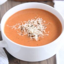 white bowl with handles filled with creamy tomato basil soup with Parmesan for topping