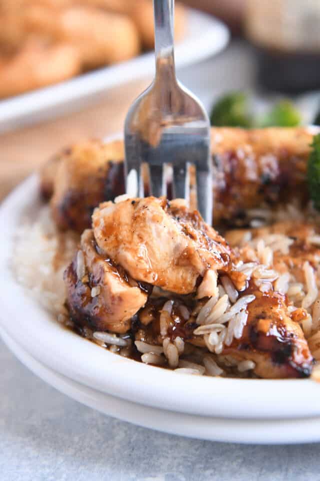 Fork with bite of saucy chicken tenders and white rice on white plate.