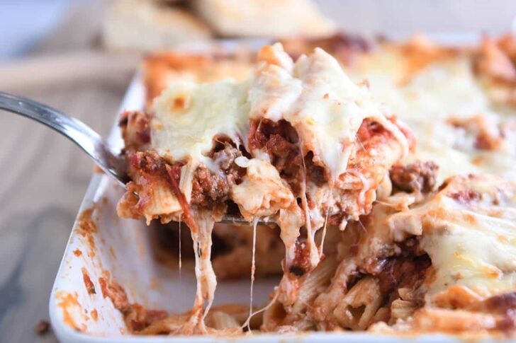 scooping serving of easy cheesy weeknight pasta bake out of white 9X13-inch pan