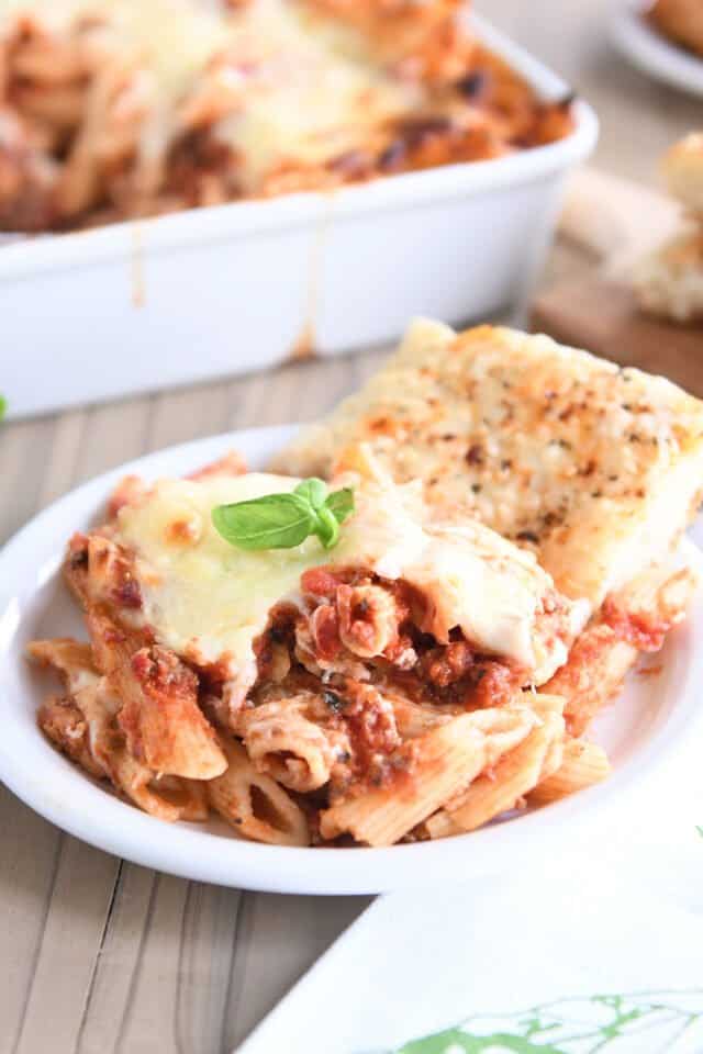 Serving of cheesy pasta bake on white plate with focaccia bread.
