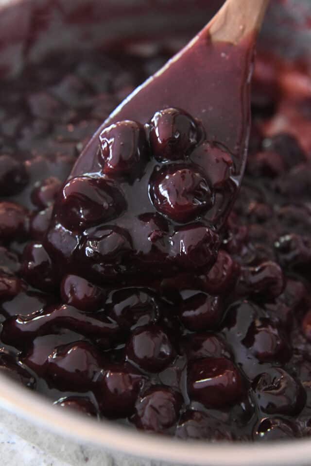 Homemade cherry pie filling with wooden spoon in pot.