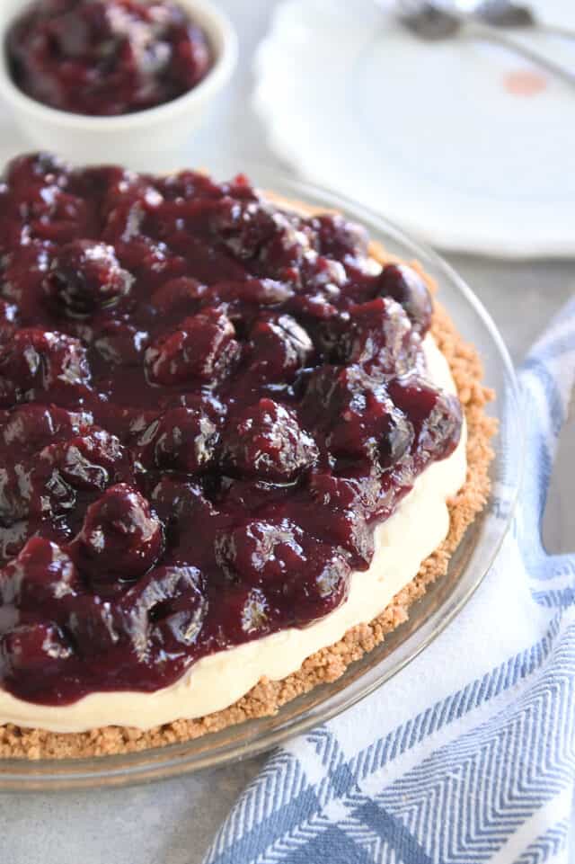 Cherry cheesecake pie in glass pie plate with blue and white towel.