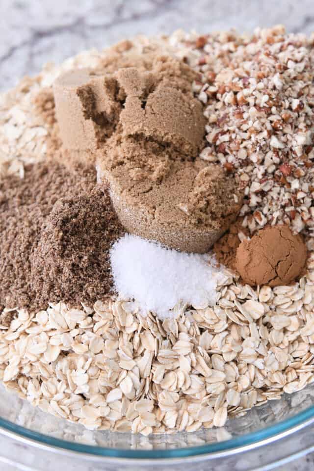 Glass bowl with oats, flax seed, salt, brown sugar, cinnamon, and pecans.